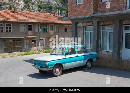 A blue retro car parked in front of dilapidated buildings under a clear sky, Zaporozhets 968, Zaporozh, Sapo, Soviet, today Ukrainian manufacturer Stock Photo