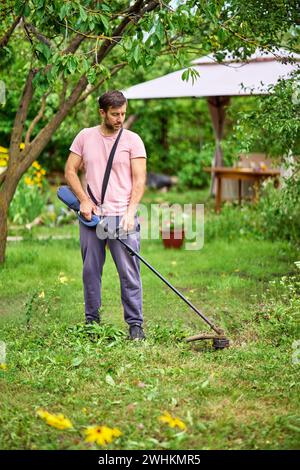 Young man cutting grass with weed cutter on his grassy lawn. Stock Photo