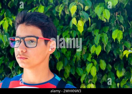 portrait for a teenager and the background is green tree with beautiful leaves while holding his bag for school or trip Stock Photo