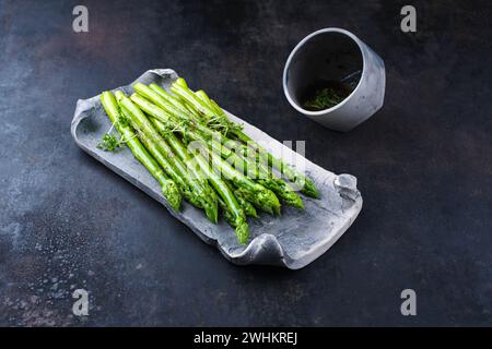 Green asparagus glazed with cress as garnish served as close-up on a design tray with text space Stock Photo