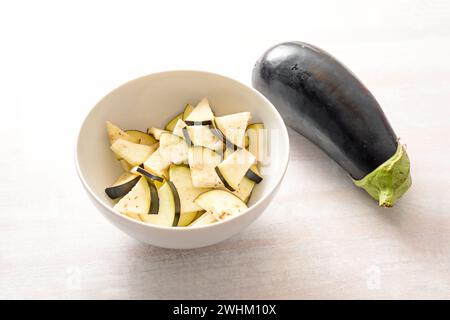 Eggplant, whole and chopped in a bowl, ingredient for various vegetable dishes, healthy vegetarian cooking concept, copy space, Stock Photo