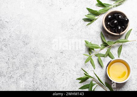 Black olives and extra virgin olive oil in little bowl with olive tree branches top view on white concrete stone background, spa Stock Photo