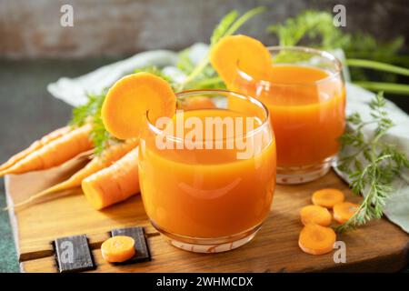 Carrot juice in a glass and fresh carrots with leaves on a stone table. Carrot healthy juice for detox. Healthy vegan vegetarian Stock Photo