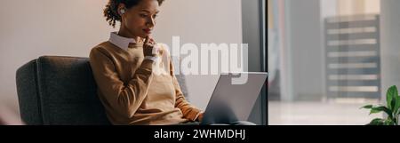 Focused female manager using laptop while sitting on cozy office background Stock Photo
