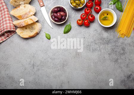 Food composition with sliced ciabatta, olives, olive oil, spaghetti, fresh basil, cherry tomatoes on gray concrete stone rustic Stock Photo