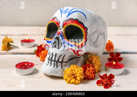 Painted human skull with burning candles and beautiful flowers for Mexico's Day of the Dead on white wooden table Stock Photo