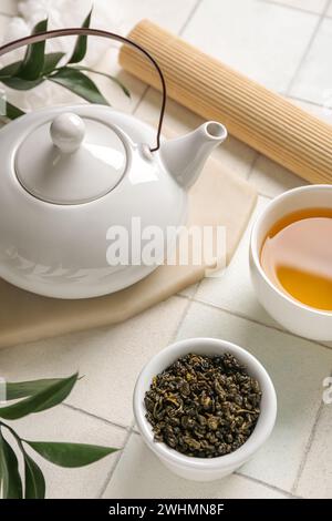 Teapot and bowl with dry leaves on white tile background, closeup Stock Photo