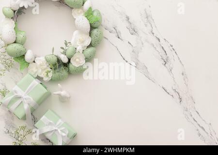 Composition with Easter wreath made of green painted eggs and bunny figurine and gifts on white table Stock Photo