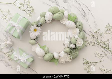 Composition with Easter wreath made of green painted eggs and bunny figurine and gifts on white table Stock Photo