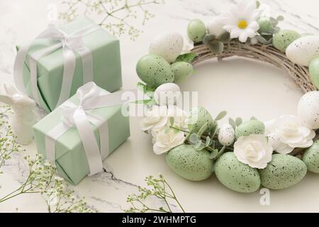 Composition with Easter wreath made of green painted eggs and bunny figurine and gifts on white table Stock Photo