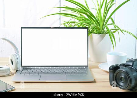 Open laptop with a blank white screen, camera, headphones and a plant on the desk of a journalist or photographer against a whit Stock Photo