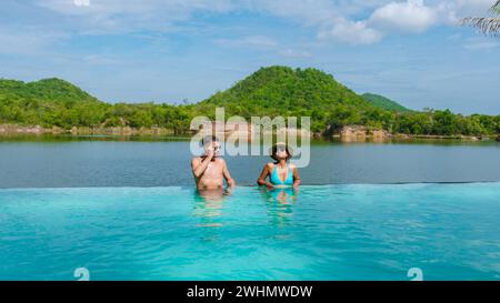 Couple on the edge of a swimming pool in Thailand looking out over the lake and green mountain Stock Photo