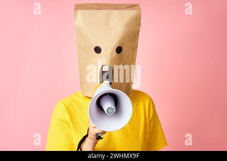 Emotional woman with paper bag on head making announcement with megaphone in hands Stock Photo