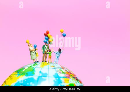 Miniature people : Happy family holding balloon on The globe with pink background Stock Photo