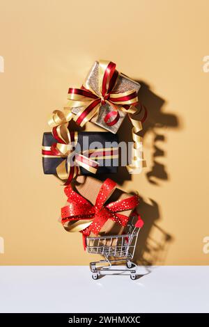 Shopping cart with gift boxes on beige gray background. Gifts wrapped in kraft paper with ribbon and bow. Holiday Shopping conce Stock Photo