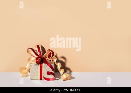 Festively wrapped gift in gold paper and ribbon with bow. Minimal Holiday Shopping backdrop Stock Photo