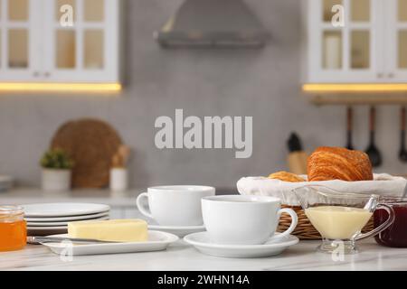 Breakfast served in kitchen. Fresh croissants, coffee, butter, jam, honey and sweetened condensed milk on white table Stock Photo