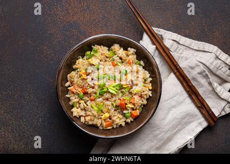 Authentic Chinese and Asian fried rice with egg and vegetables in ceramic brown bowl top view, dark rustic concrete table backgr Stock Photo