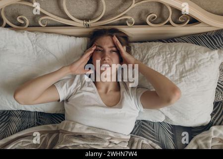 Young woman with headache flu ill sick disease cold at home indoor lying on bed. Stock Photo