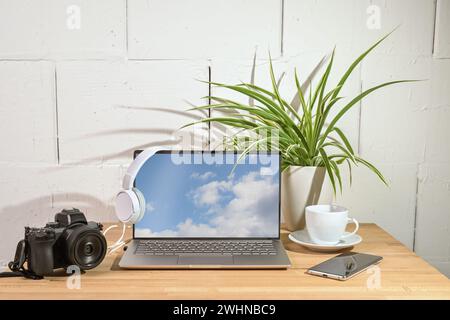 Laptop, camera, headphones and smart phone on a wooden desk, office workplace of a journalist or photographer against a white pa Stock Photo