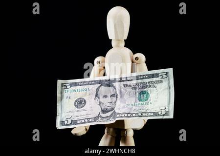 Wooden dummy and five dollars banknote, business concept, puppet made of wood, art mennequin.Wooden Doll Stock Photo