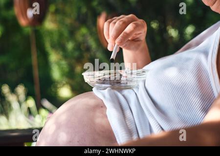 Pregnant women smoking with ashtray on stomach Stock Photo