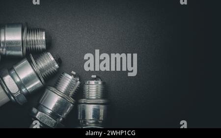 Four spark plugs arranged in a semicircle on a gray gradient background. Stylized photo. Stock Photo