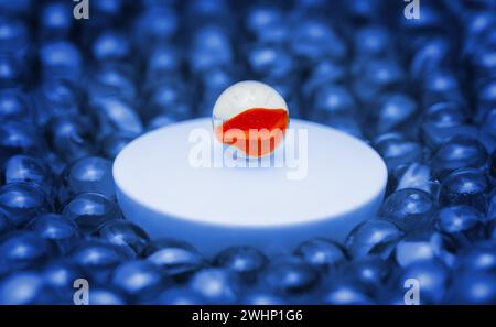 A colored glass ball on a podium surrounded by plain glass balls. Macro photography with shallow depth of field. Concept of public speaking, lecture, Stock Photo