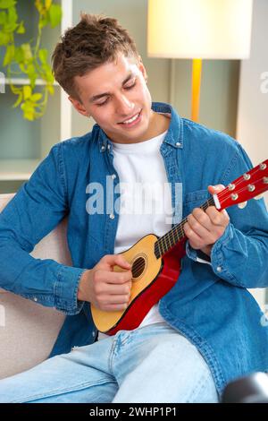 Vertical portrait Attractive young man playing ukulele on the sofa.interior Stock Photo