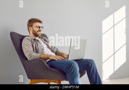 Happy, relaxed young man sitting in armchair and watching video on laptop computer Stock Photo