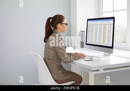 Female bookkeeper sitting at table, making financial report in spreadsheet Stock Photo