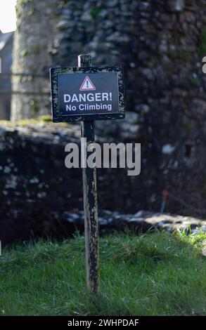 Black, danger sign in front of an old, stone city wall around a castle on the green grass Stock Photo