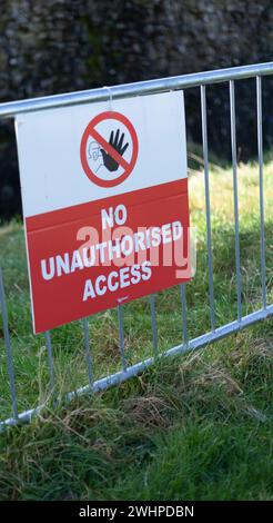 No Unauthorised Access Sign on a metal fence on the grass in front of an old, stone wall Stock Photo