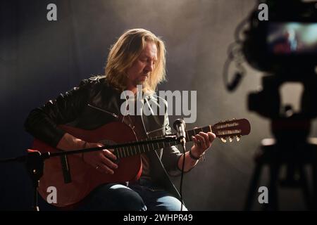 Portrait of long haired mature musician playing acoustic guitar with camera recording video copy space Stock Photo