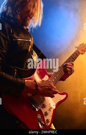 Ambient vertical portrait of long haired rock musician playing electric guitar on stage in nightclub Stock Photo