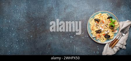 Italian seafood pasta spaghetti with mussels, shrimps, clams in tomato sauce with green basil on plate on rustic blue concrete b Stock Photo