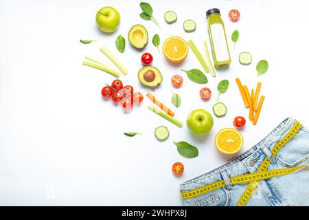Fresh fruit, vegetables, smoothie falling into jeans and yellow measuring tape instead of belt on white background. Concept of w Stock Photo