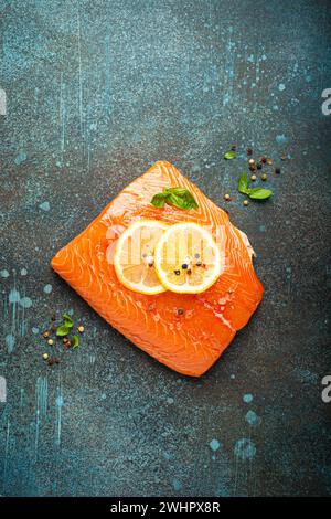 Fresh raw salmon marbled fillet on dark blue rustic concrete table background with lemon, coarse salt, green herbs top view. Hea Stock Photo