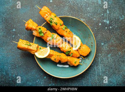 Grilled barbecue salmon skewers seasoned with green parsley and lemon on ceramic plate on dark blue concrete rustic table backgr Stock Photo