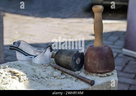 Tools from a stonemason, consisting of plastic coated wooden mallets, chisel and safety goggles on a gray stone, traditional cra Stock Photo