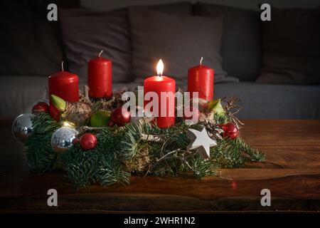 Advent wreath with one burning red candle and Christmas decoration on a wooden table in front of the couch, festive home decor f Stock Photo