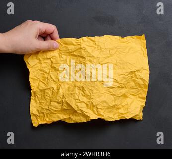 A woman's hand holds a yellow crumpled sheet of paper Stock Photo