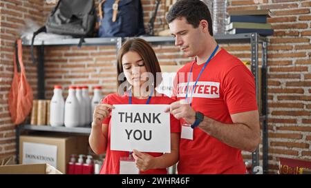 Man and woman volunteers standing together holding paper with thank you message at charity center Stock Photo