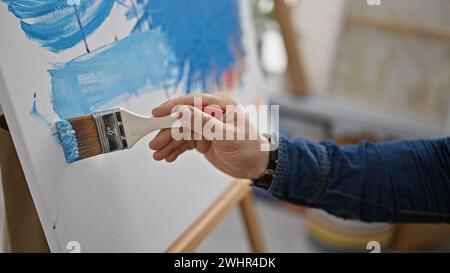 Handsome hispanic man, an aspiring artist, passionately drawing on canvas with a brush in an art studio filled with creativity Stock Photo