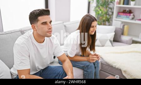 A contemplative couple sits apart on a sofa in their modern living room, depicting potential relationship issues. Stock Photo