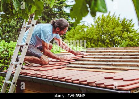 Roofer at work, installing clay roof tiles. back garden with shed, summer house garden Stock Photo