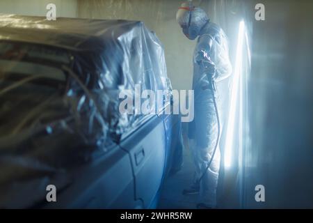 Car painter in protective clothes and respirator mask painting vehicle Stock Photo