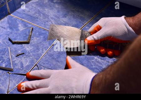 Close-up of the hands of the master, who remove the broken tiles from the floor with a tool. Stock Photo