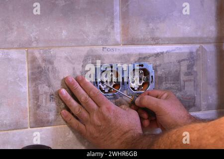 The picture shows the hands of a man who are holding a screwdriver with which he repairs sockets. Stock Photo