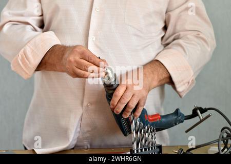 In the picture, a man who holds a drill with one hand, and clamps the drill in the drill with the other key. Stock Photo